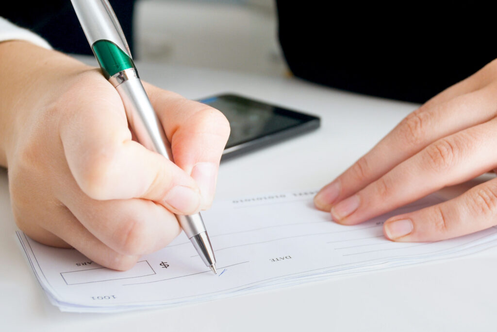 image of a person's hands while they sign a check.