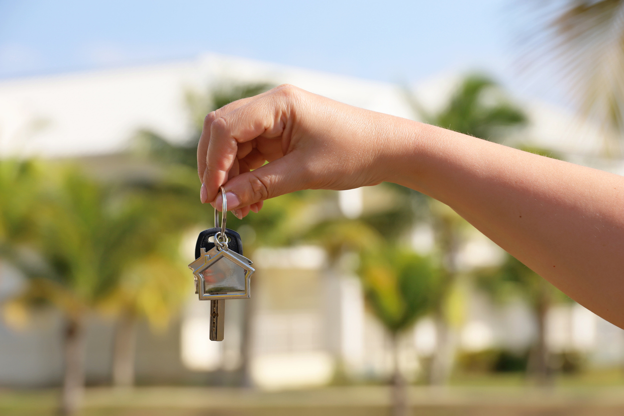 hand hlds up keys with home shaped keychain in front of house in florida - best time to buy a house in florida