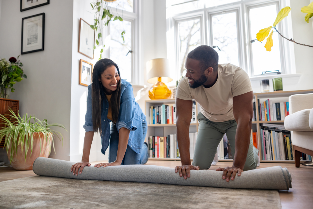New homeowners arranging a rug in their living room after moving into a home.
